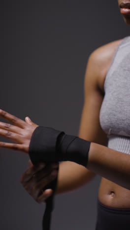 Vertical-Video-Close-Up-Studio-Shot-Of-Woman-Putting-On-Boxing-Wraps-On-Hands-Before-Exercising